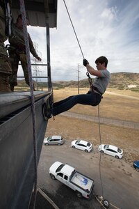 A high school student starts to rappel down the side of a tower.