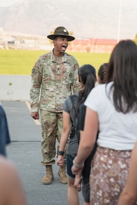 A drill sergeant sings a cadence in front of a formation of high school students.