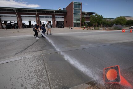 Two high school students use a firehose to spray a road cone