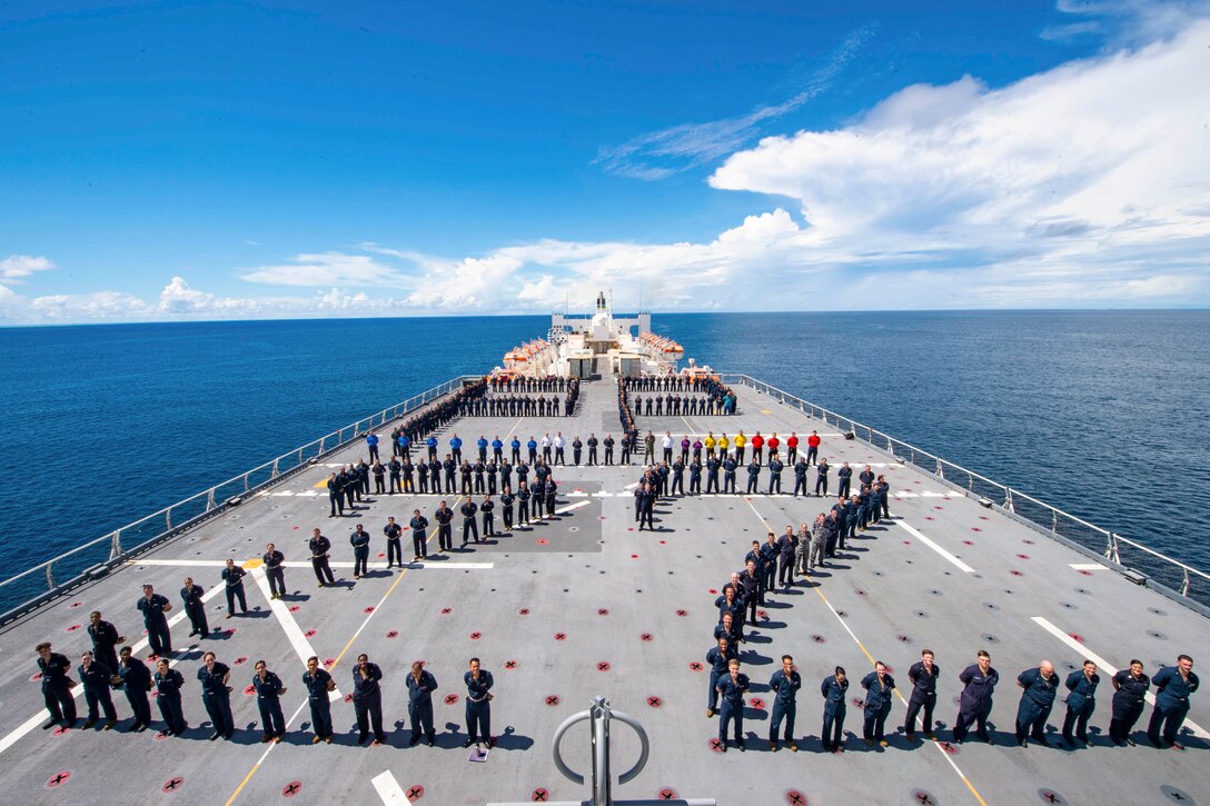 Sailors stand in lines to form two letter p’s and the number 22 on a ship at sea.