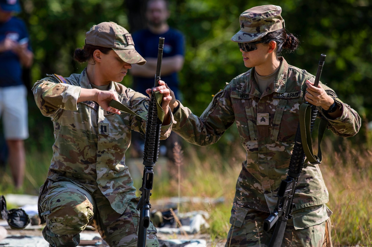 A soldier holding a weapon helps a fellow soldier with a weapon during a competition.