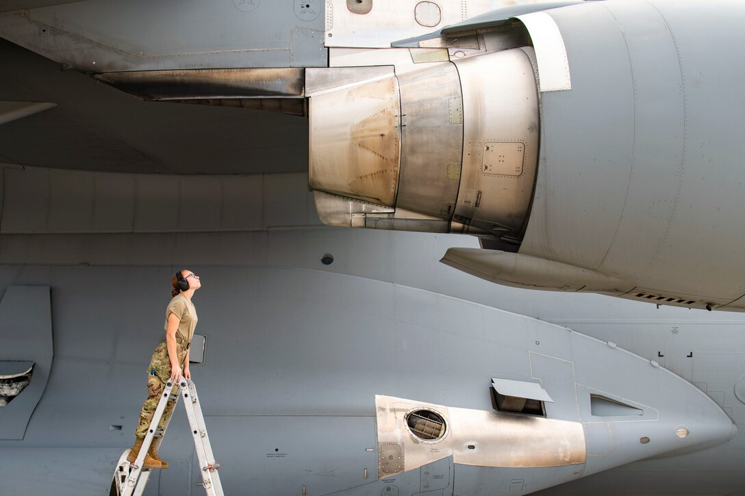 An airman standing on a ladder inspects an aircraft.