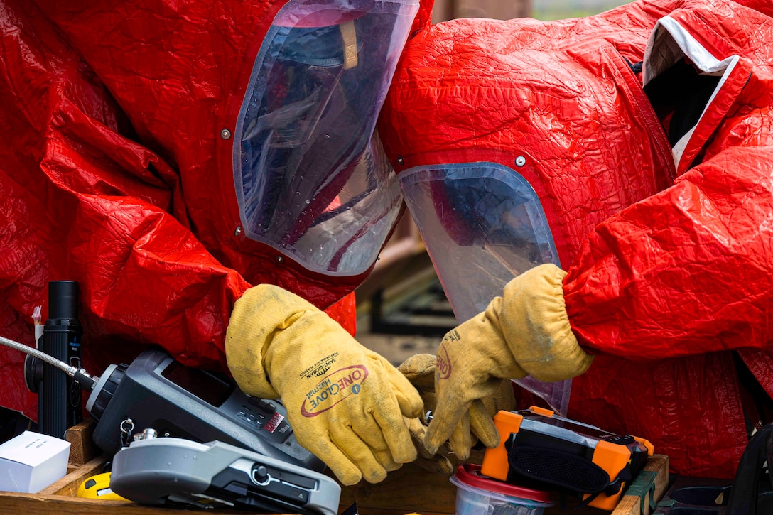 Two people in hazmat suits work with equipment.