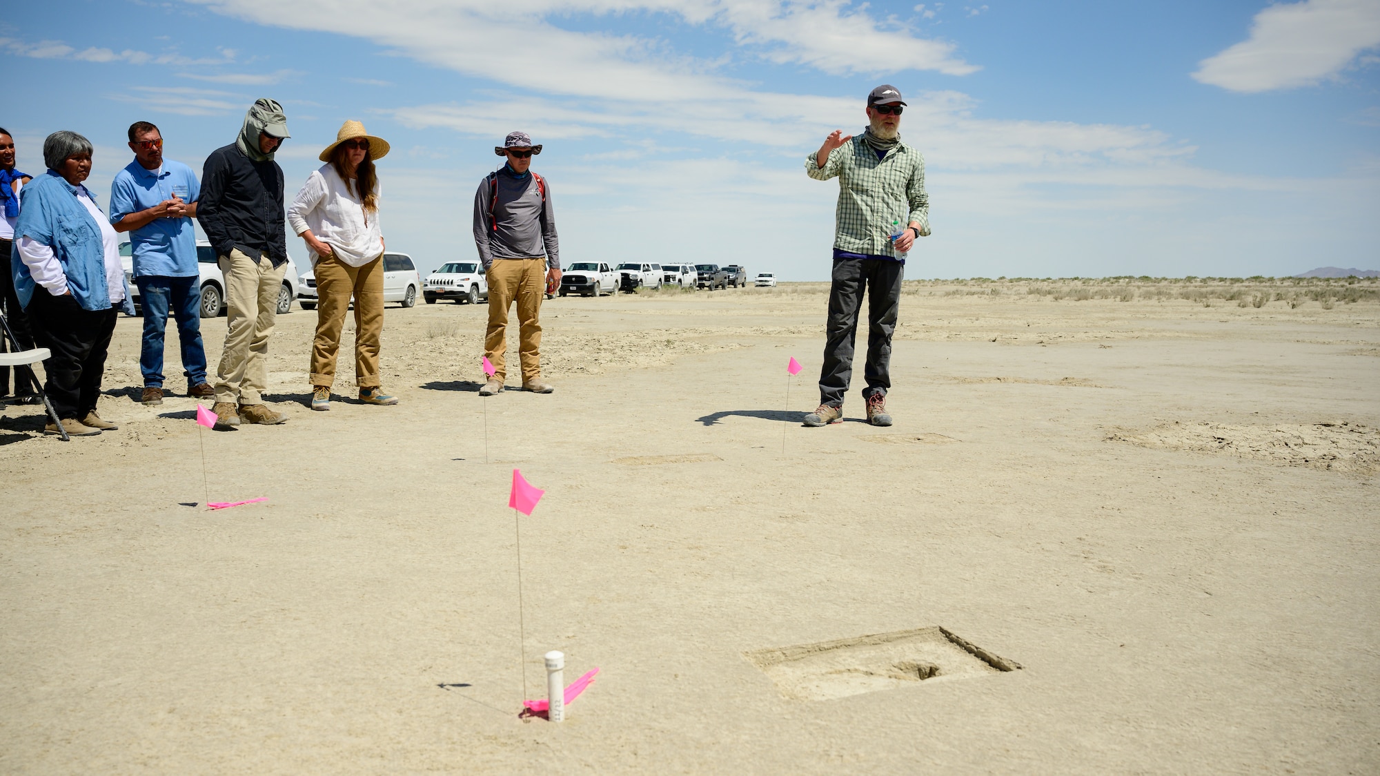 A footprint appears on an archaeological site marked with a pink pin flag with Daron Duke and others in the background.