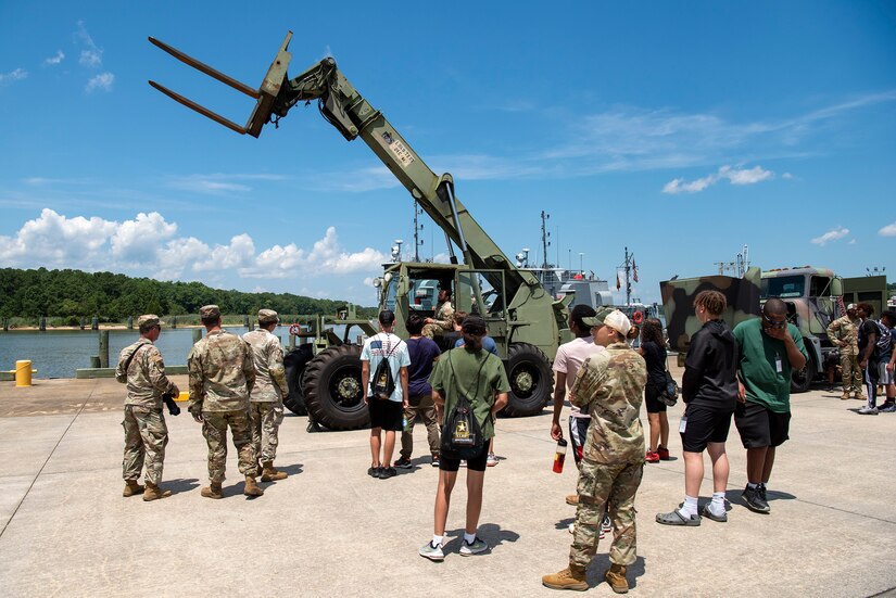 Soldiers demonstrate how to use heavy machinery in front of high school students.