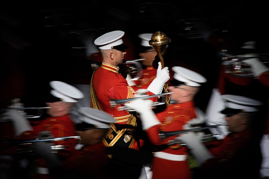 Marines in formal uniforms play instruments in formation in a semi-blurred picture.