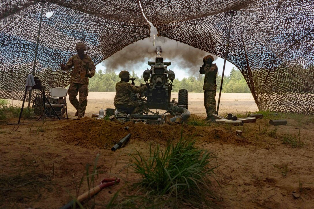 Soldiers fire a weapon under a tent.