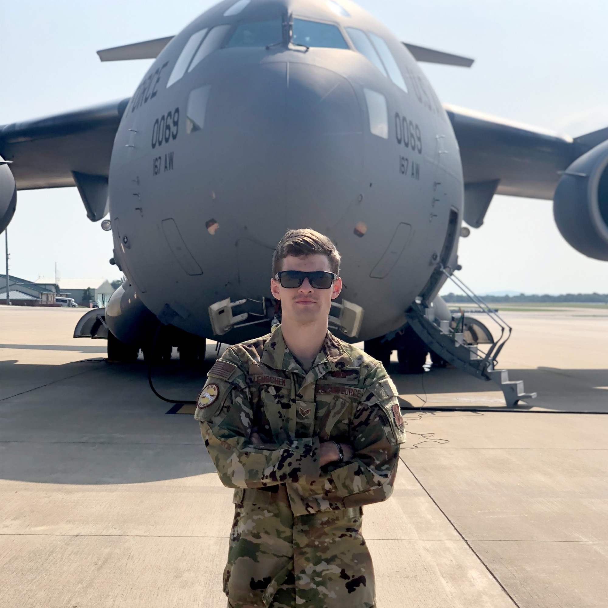 Staff Sgt. Kyle Leuschen a loadmaster for the 167th Airlift Squadron, stands in front of a C-17 Globemaster III aircraft.