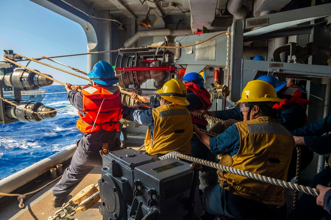 Sailors use ropes to pull a fuel hose.