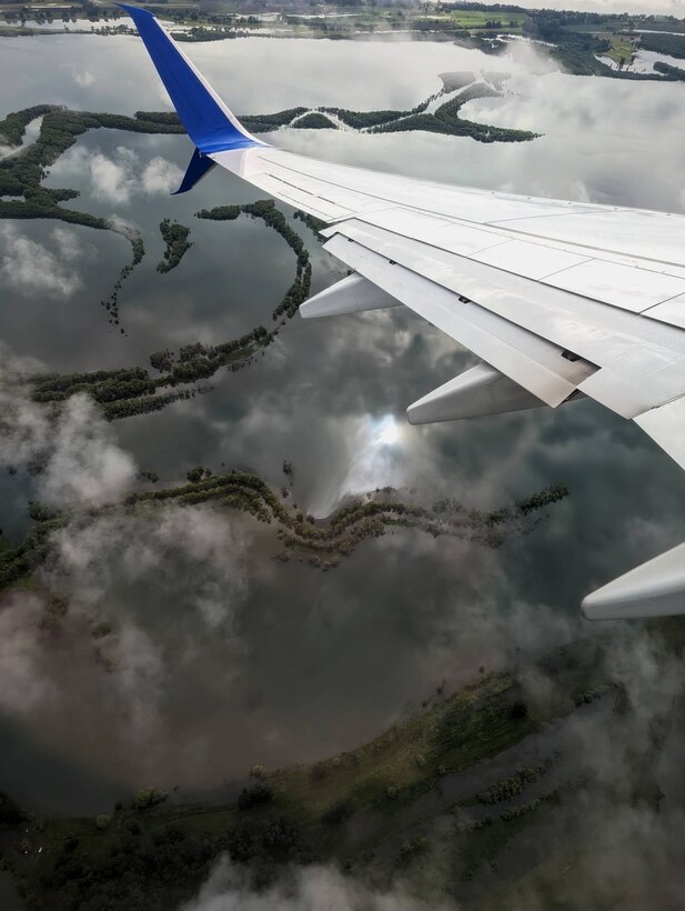 An aerial of the lower Columbia River near Portland, June 11, 2022. You can see the white wing of the airplane that angles left. below is the Lower Columbia River Basin swollen with deep blue water and inundated trees.