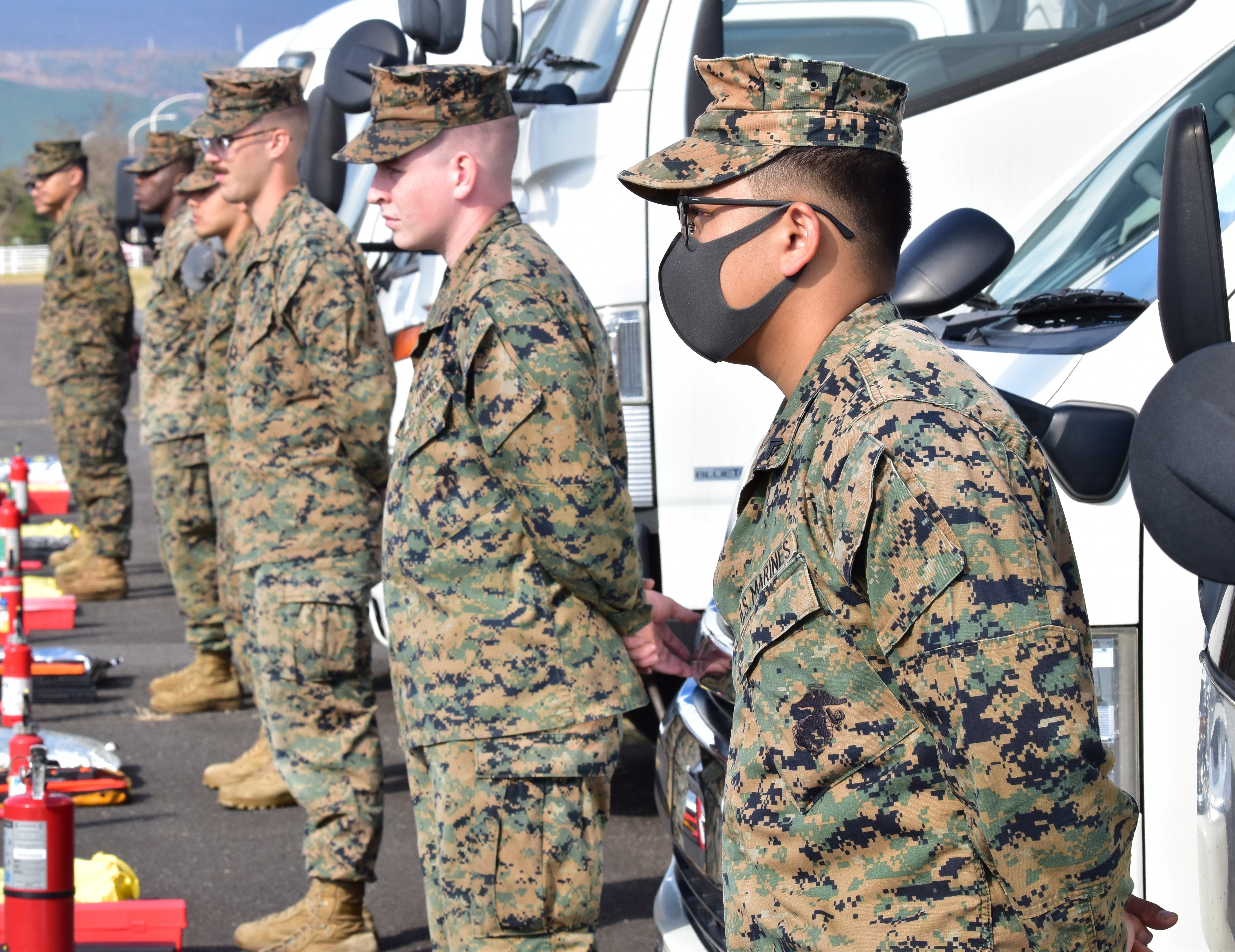 Six Marines in uniform standing at attention in a parking lot.
