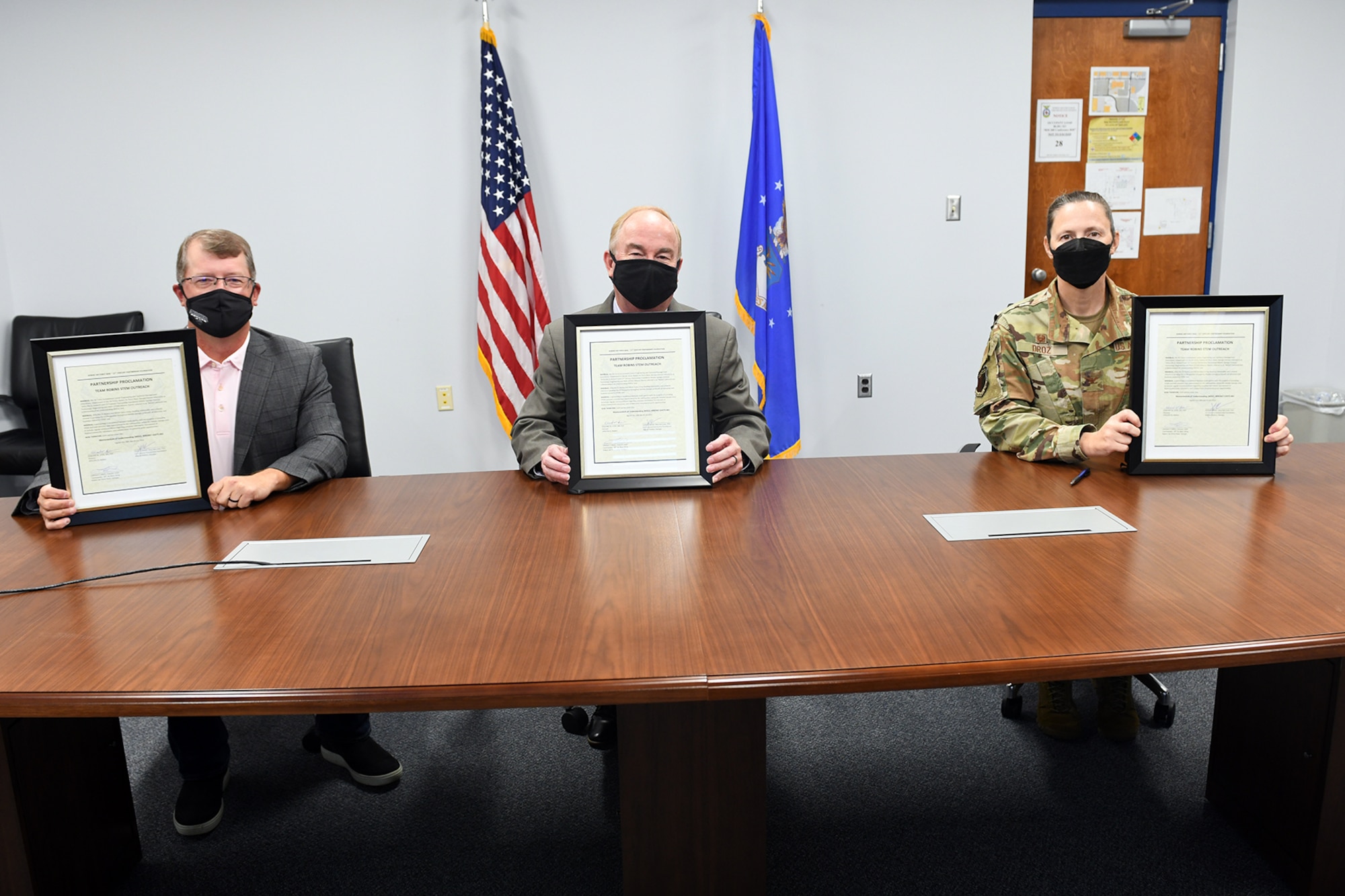 Photo shows three people sitting at table holding up papers showing signed papers.