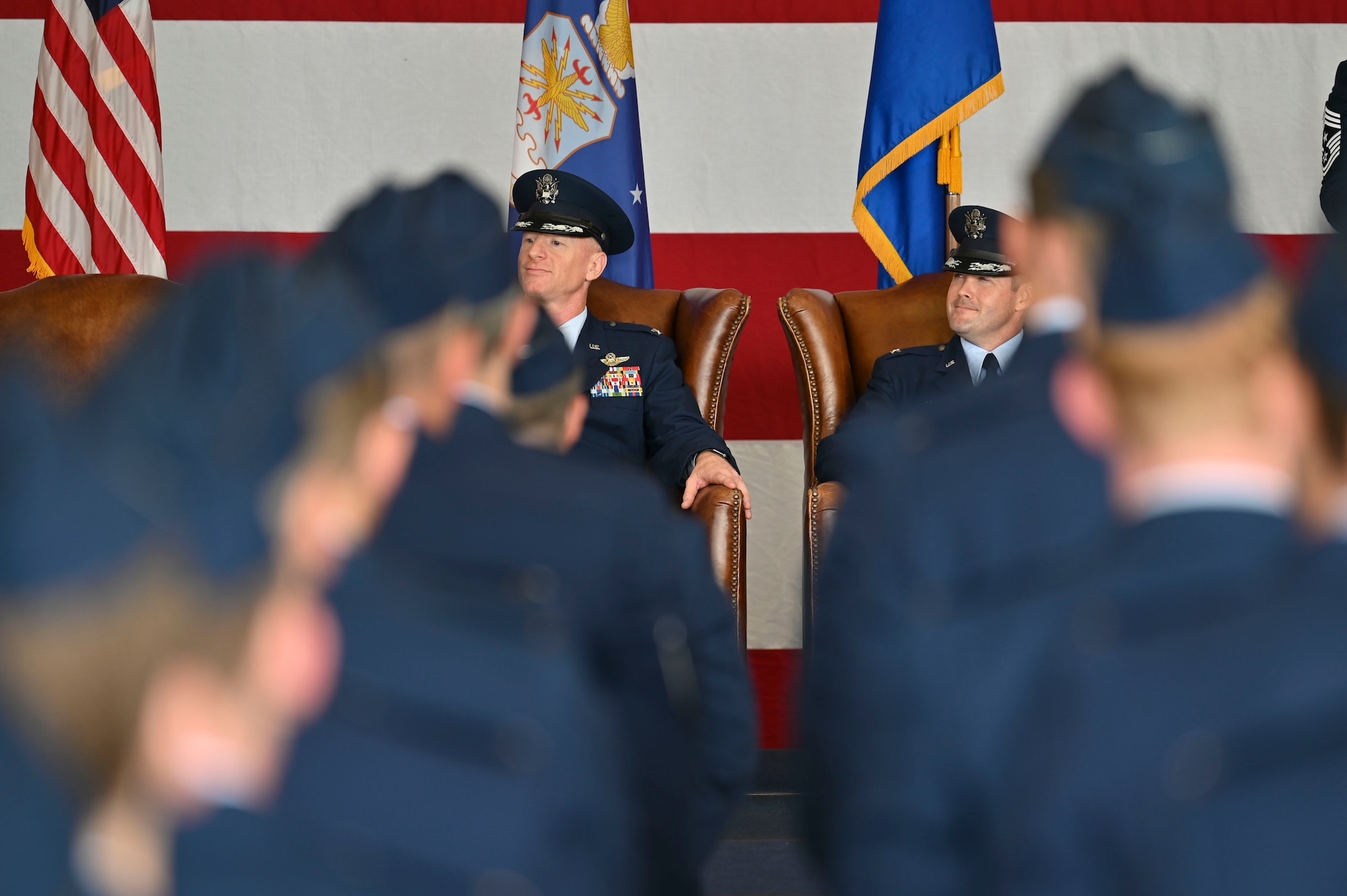 U.S. Air Force Col. Seth Graham, outgoing 14th Flying Training Wing commander and Col. Justin Grieves, incoming 14th FTW commander, listen as Maj. Gen. Craig Wills, 19th Air Force commander, speaks to the crowd at the Change of Command ceremony on Columbus Air Force Base, Miss., July 22, 2022. The Colonels share similar backgrounds, as they were both previous bomber pilots in their careers. (U.S. Air Force photo by Senior Airman Jessica Haynie)
