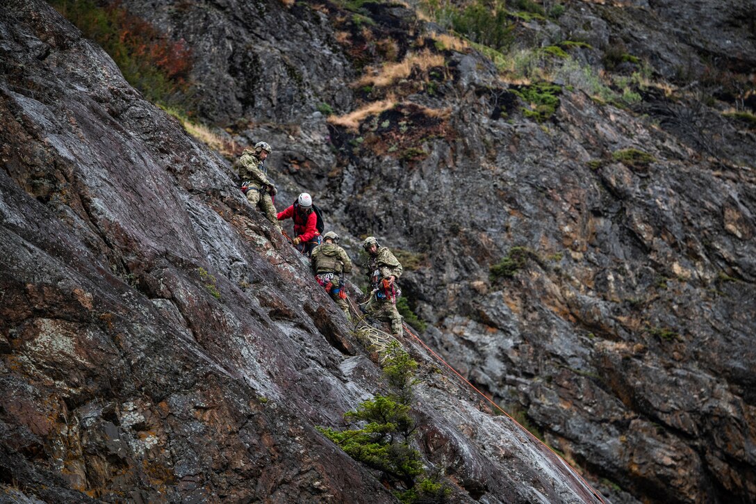 Airmen scale a steep cliff face.