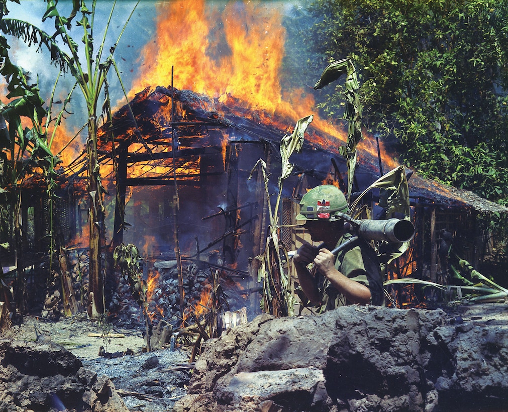 Private First Class Raymond Rumpa, C Company, 3rd Battalion, 47th Infantry, 9th Division, with 90mm recoilless rifle, walks by as Viet Cong base camp burns, My Tho, Vietnam, April 5, 1968 (U.S. Army/National Archives and Records Administration/Dennis Kurpius)