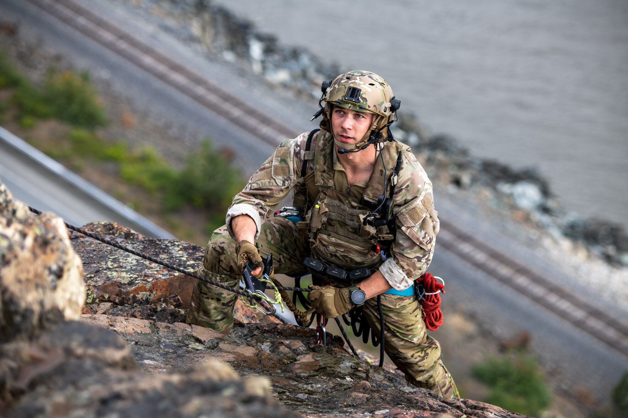 An Airman grips a rope as he hangs off of a cliff face.
