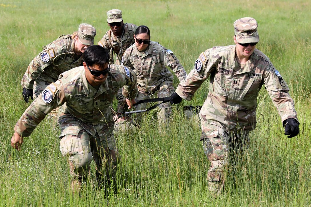 Soldiers carry a stretcher through a field.