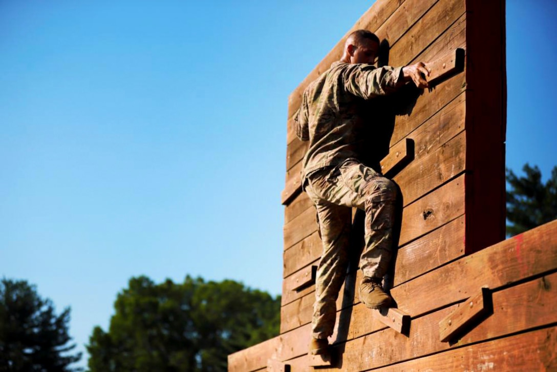A soldier climbs a wall during an outdoor competition.