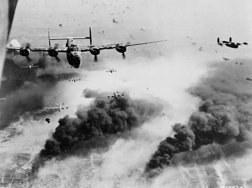 Bomber aircraft fly in the sky above plumes of black smoke.