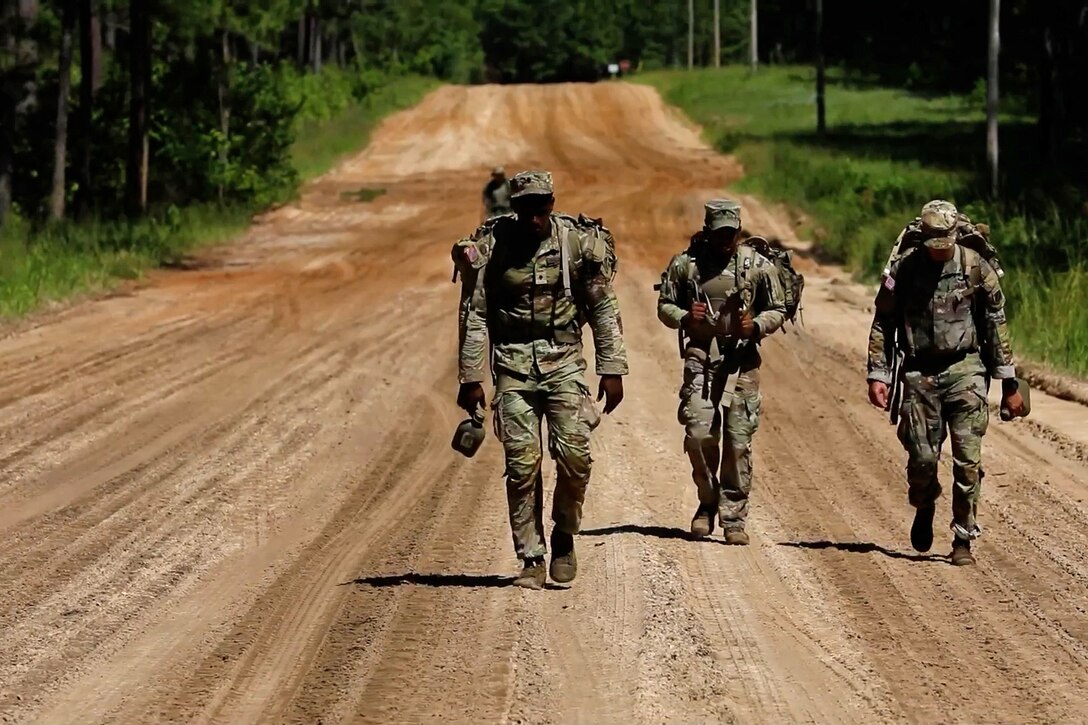 Three soldiers walk along a dirt road in the woods.