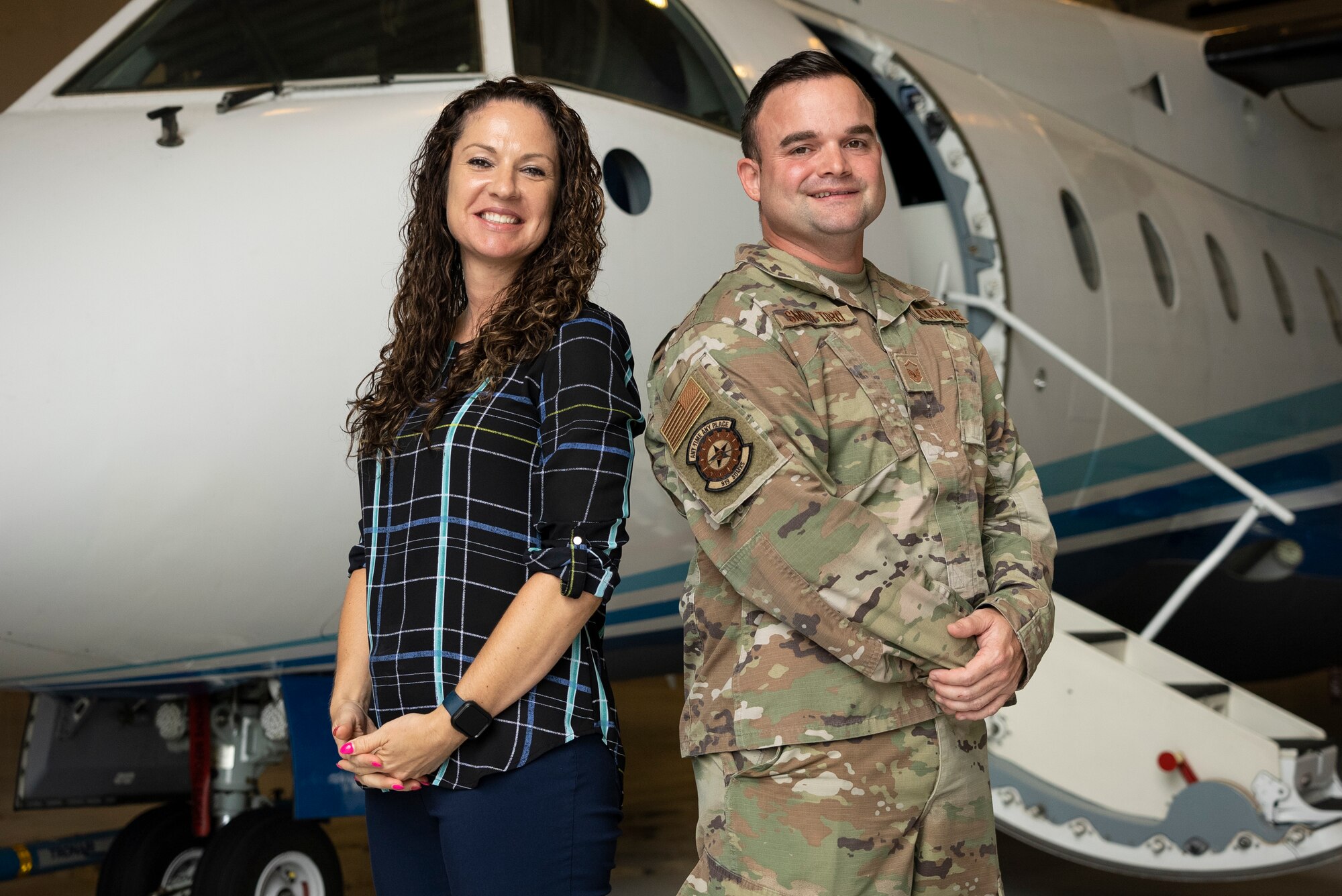 Civilian and Airman stand back-to-back in front of aircraft.