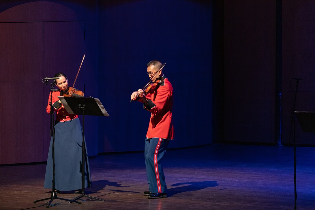 Violinists Staff Sgt. Sara Matayoshi and Staff Sgt. Foster Wang perform Alfred Schnittke's Moz-Art, complete with blue lighting on stage on July 23, 2022. (U.S. Marine Corps photo by Staff Sgt. Chase Baran/released)