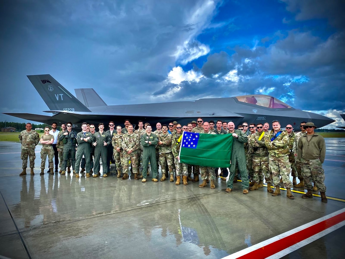 Airmen assigned to the Vermont Air National Guard’s 158th Fighter Wing hold a Green Mountain Battle flag in front of their U.S. Air Force F-35A Lighting II after successfully completing an Agile Combat Employment exercise to support the NATO air shielding mission at Amari Air Base, Estonia, July 15, 2022. Exercises and engagements in the European area of responsibility demonstrate U.S. commitment to the security and stability in this region.