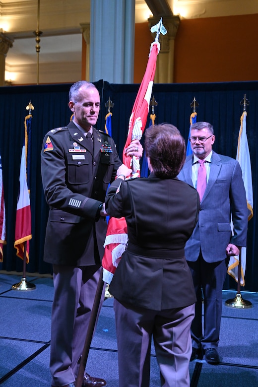 Military male officer takes unit flag from female military officer in a military change of command ceremony.