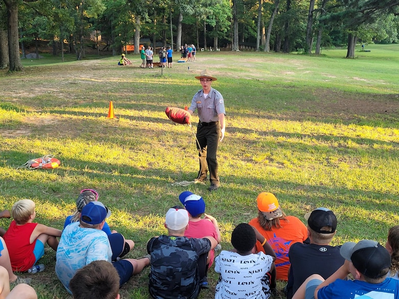 Ranger Nathan Herd stands in front of several children in a field demonstrating to the campers at Camp Currie conservation camp how to toss a type 4 personal floatation device to someone in the water. (USACE Photo by WES DAVENPORT)