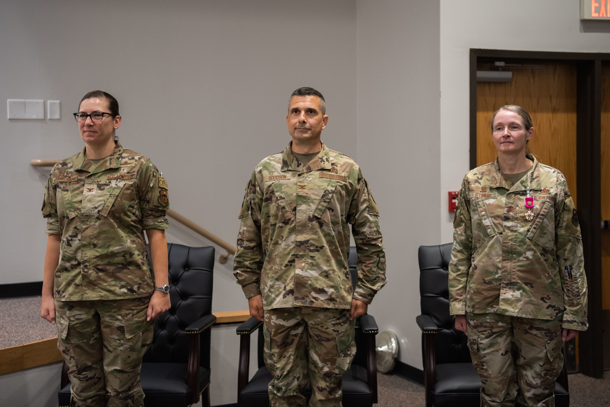 Three people are standing at attention in front of their seats