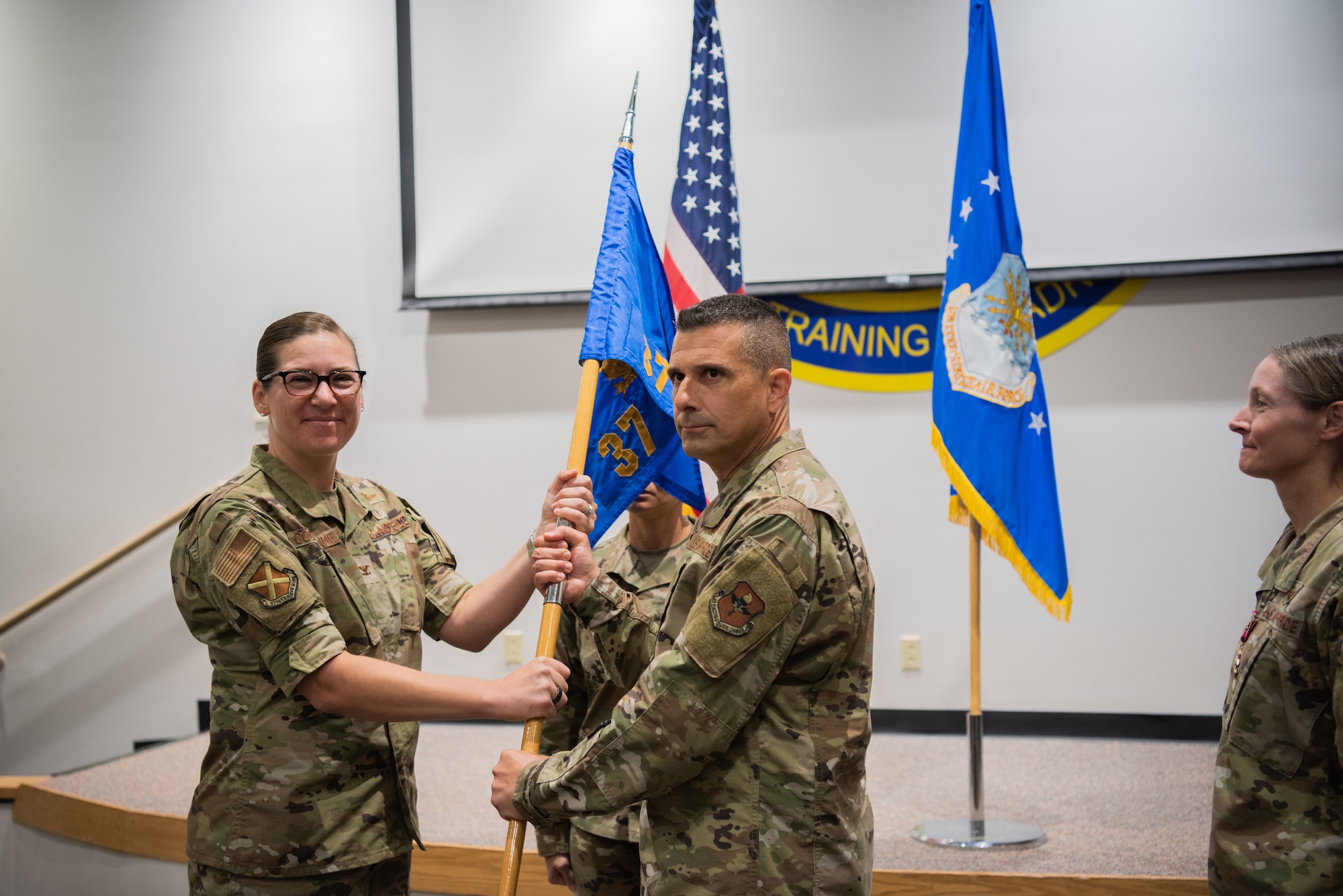 Two people hold onto a guidon and they are looking at cameras posing