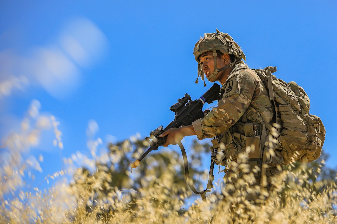 A soldier holds a weapon while standing in a field.