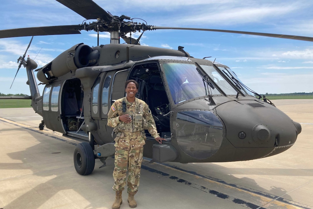 A soldier stands in front of a helicopter.