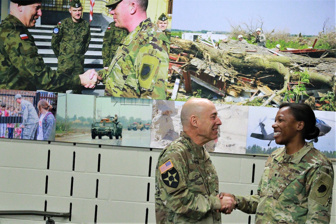 A man and woman shake hands in front of a large mural.