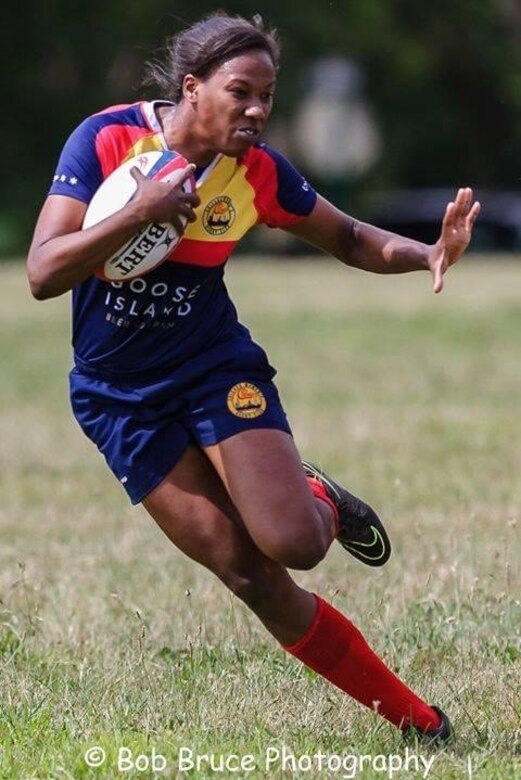 A woman runs with a rugby ball.