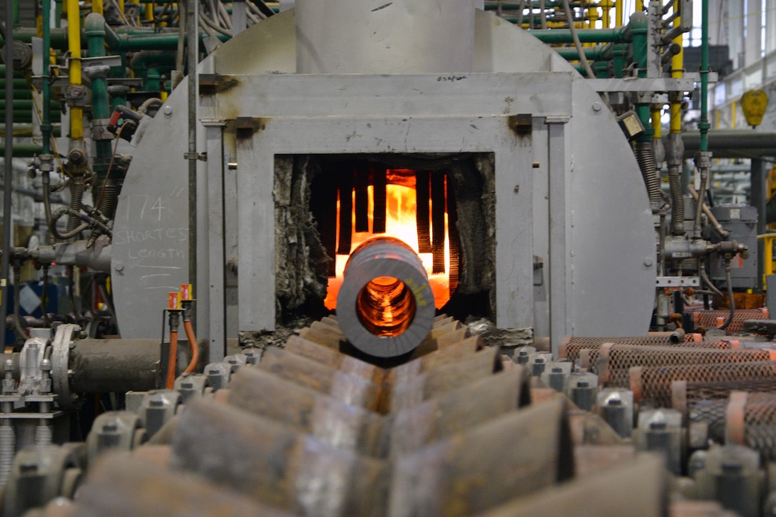 A large metal tube rolls into a furnace.