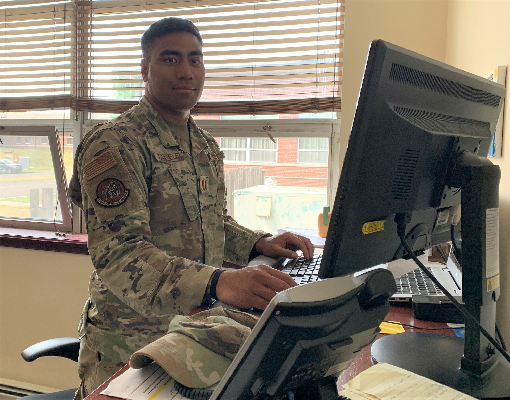 Man in military uniform standing at desk in front of computer.