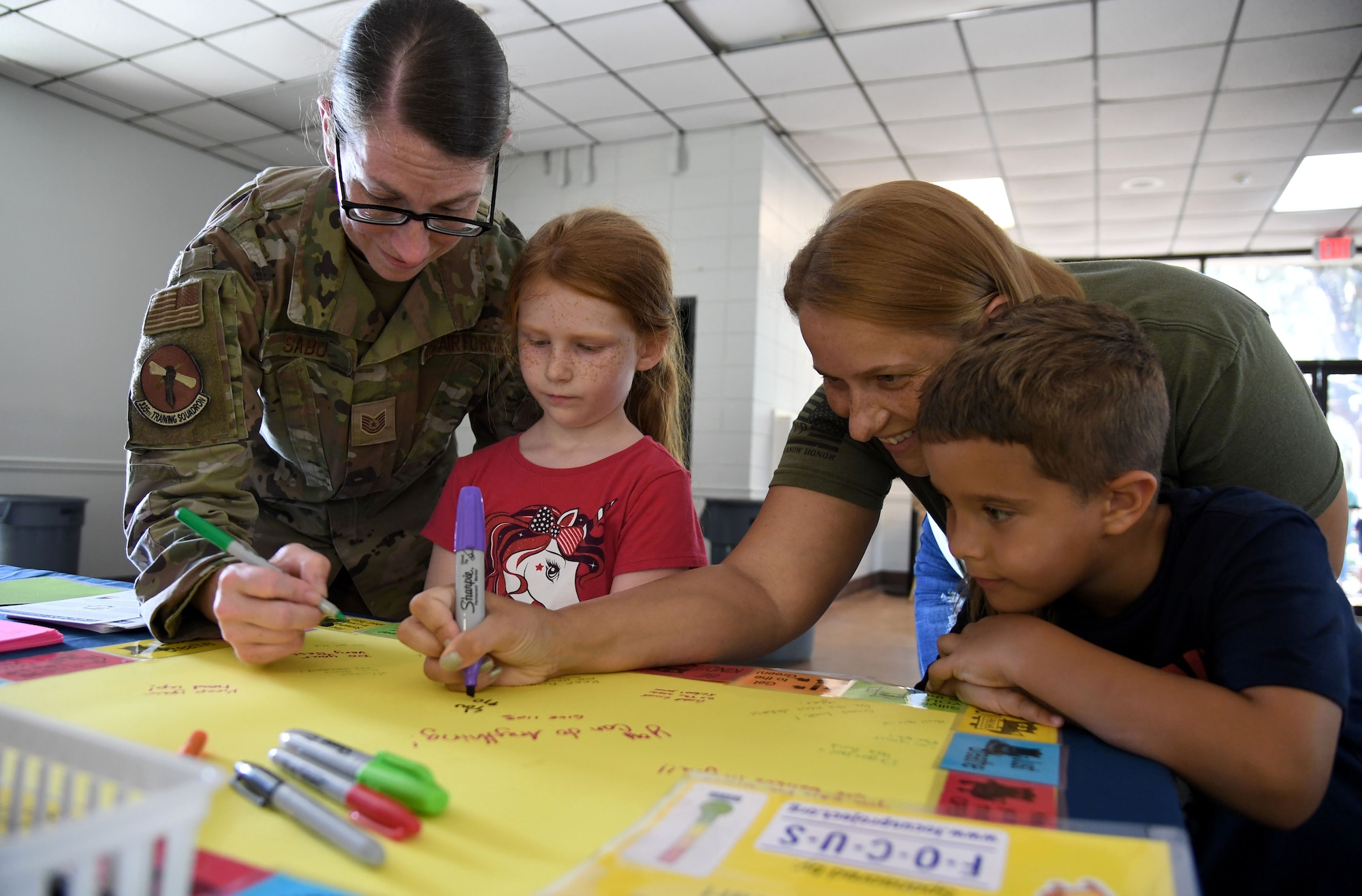 Keesler families sign a poster board during a Back to School Bash at the Keesler Marina on Keesler Air Force Base, Mississippi, July 28, 2022. The bash, a collaboration of agencies that included Operation Homefront, the Back-to-School Brigade and Keesler support agencies, provided families with nearly 200 bookbags filled with supplies and included games and free snow cones. (U.S. Air Force photo by Kemberly Groue)