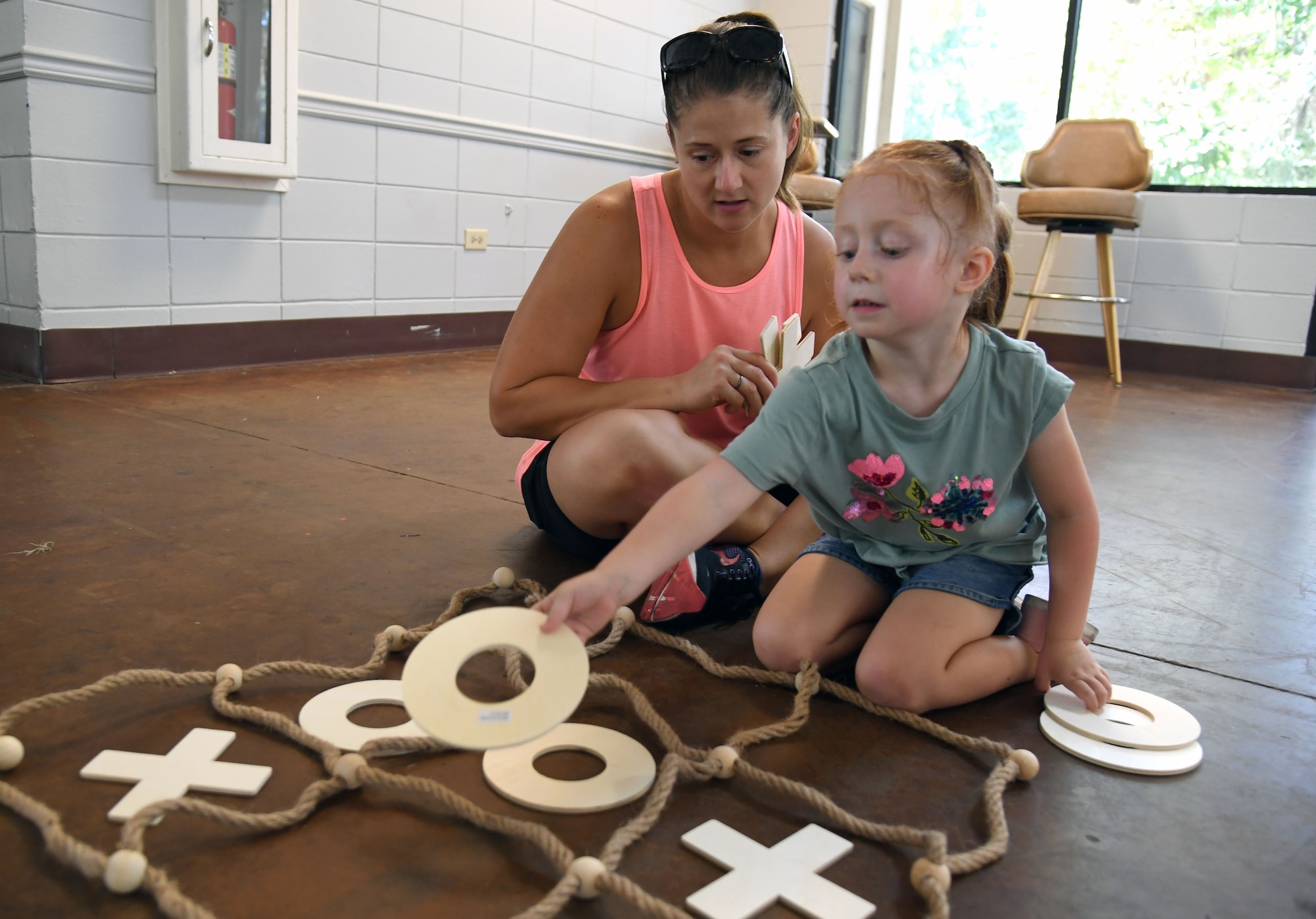 Jennifer Dykes, wife of U.S. Air Force Lt. Col. Barrington Dykes, 81st Dental Squadron orthodontist, and their daughter, Norah, play a game of tic-tac-toe during a Back to School Bash at the Keesler Marina on Keesler Air Force Base, Mississippi, July 28, 2022. The bash, a collaboration of agencies that included Operation Homefront, the Back-to-School Brigade and Keesler support agencies, provided families with nearly 200 bookbags filled with supplies and included games and free snow cones. (U.S. Air Force photo by Kemberly Groue)