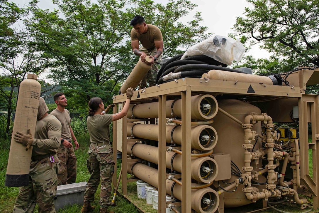 An airman hands parts of a water filtration system to others on the ground.