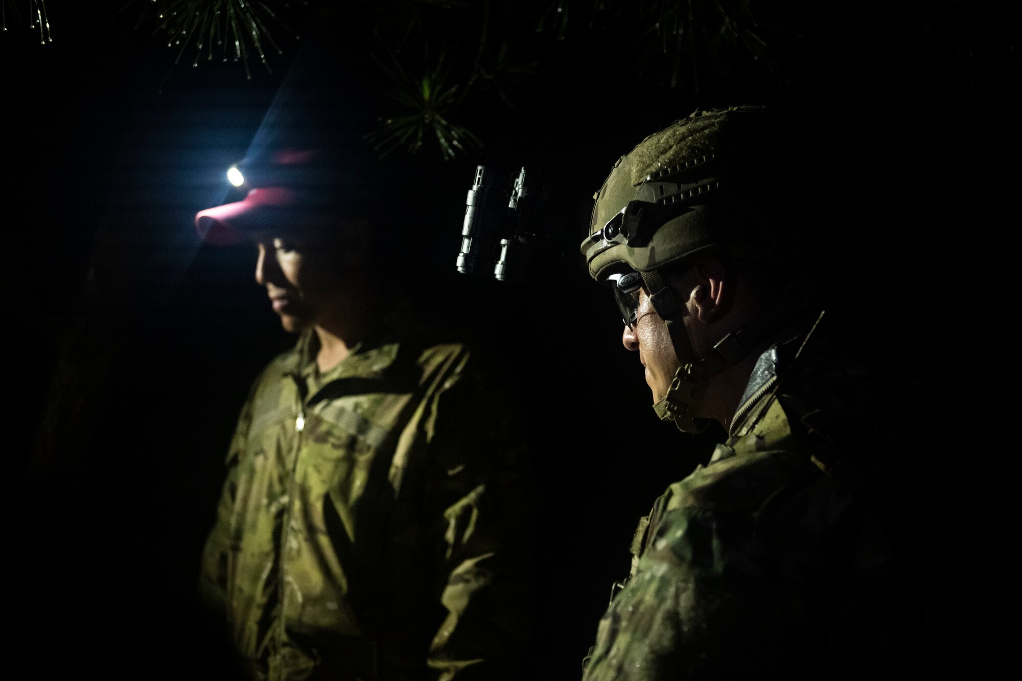 U.S. military members in tactical gear stands on a dark trail.