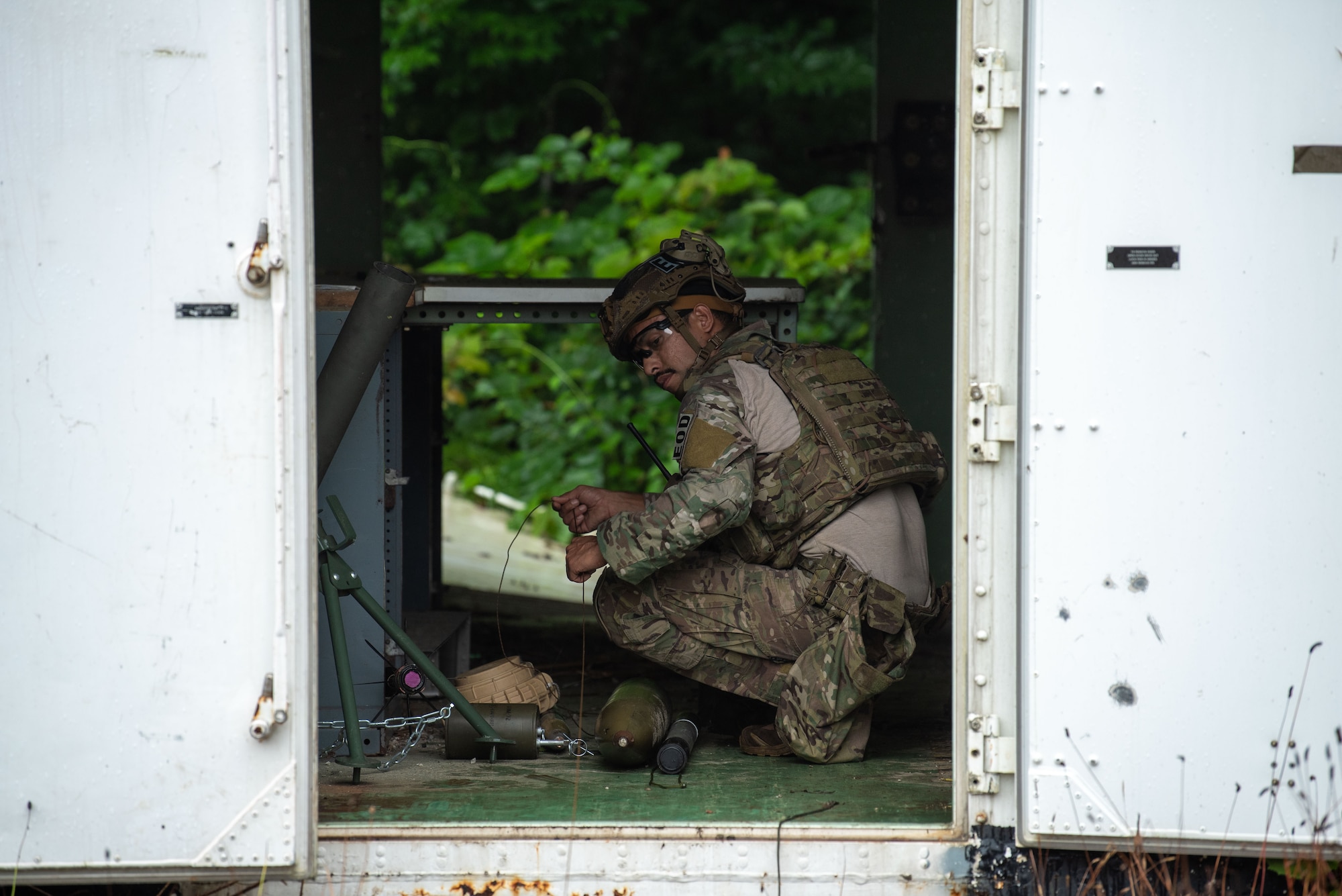 U.S. military member in tactical gear guides a line of wire towards an explosive ordnance.