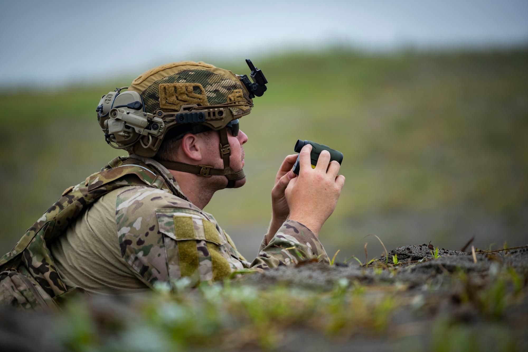 U.S. military member in tactical holds binoculars.