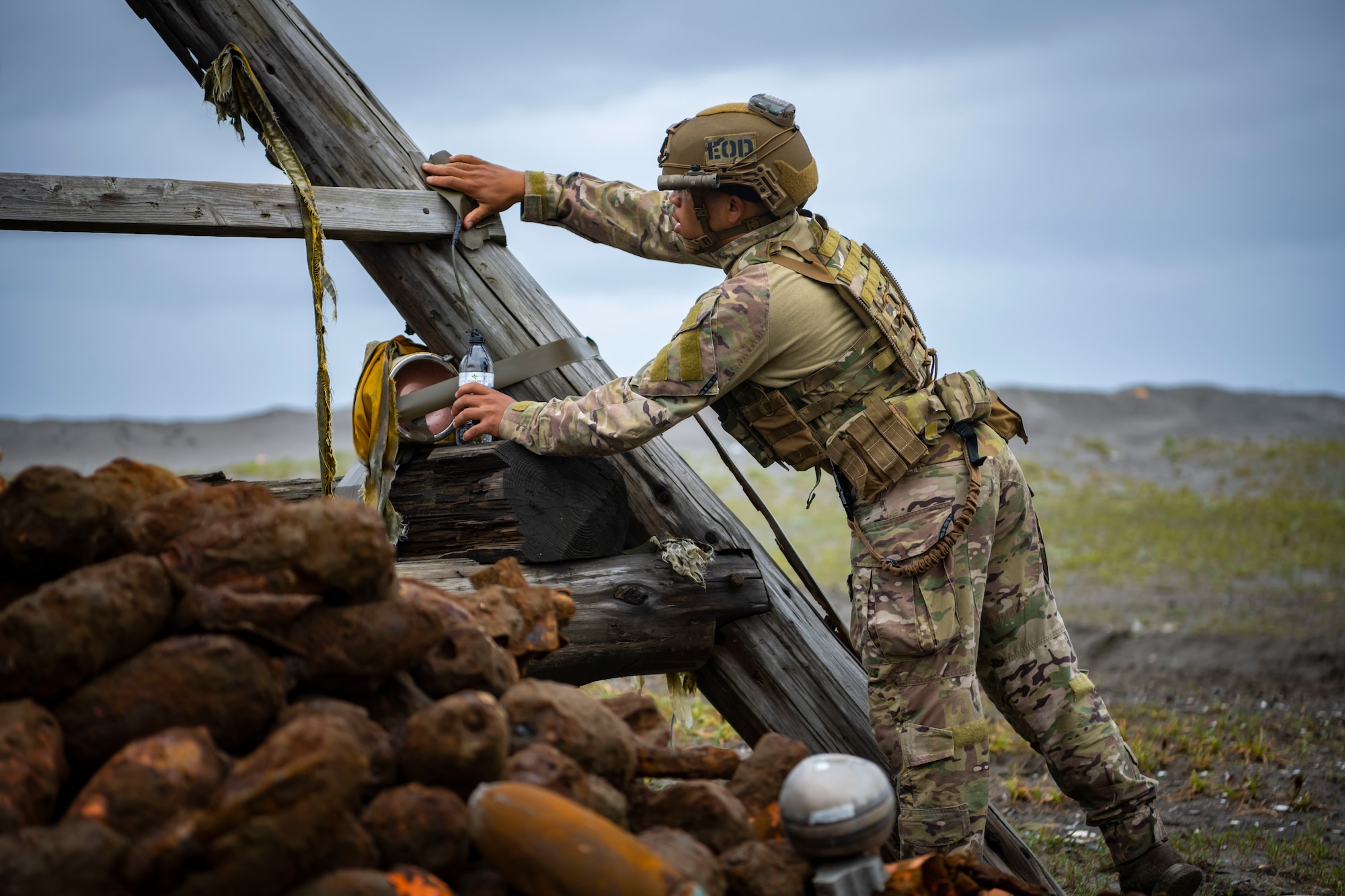 U.S. military member in tactical gear plants an explosive on a wooden post.