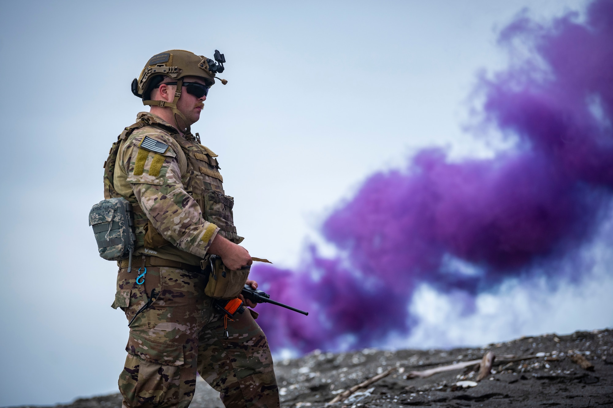 U.S. military member in tactical gear calls in a medical evacuation on the radio as purple smoke spreads in the sky.