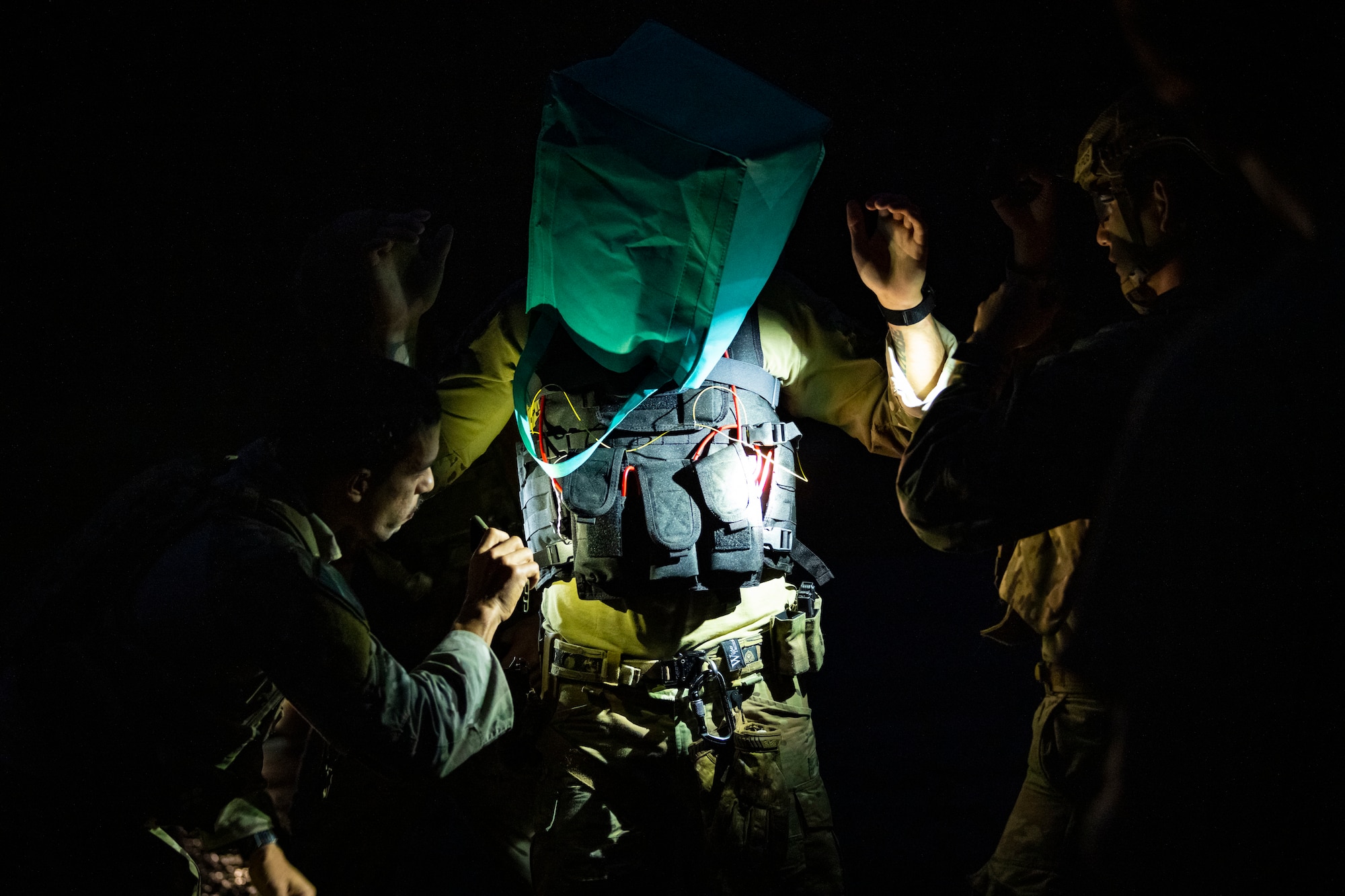 U.S. military members hold flashlights while disarming a suicide vest on a volunteer.