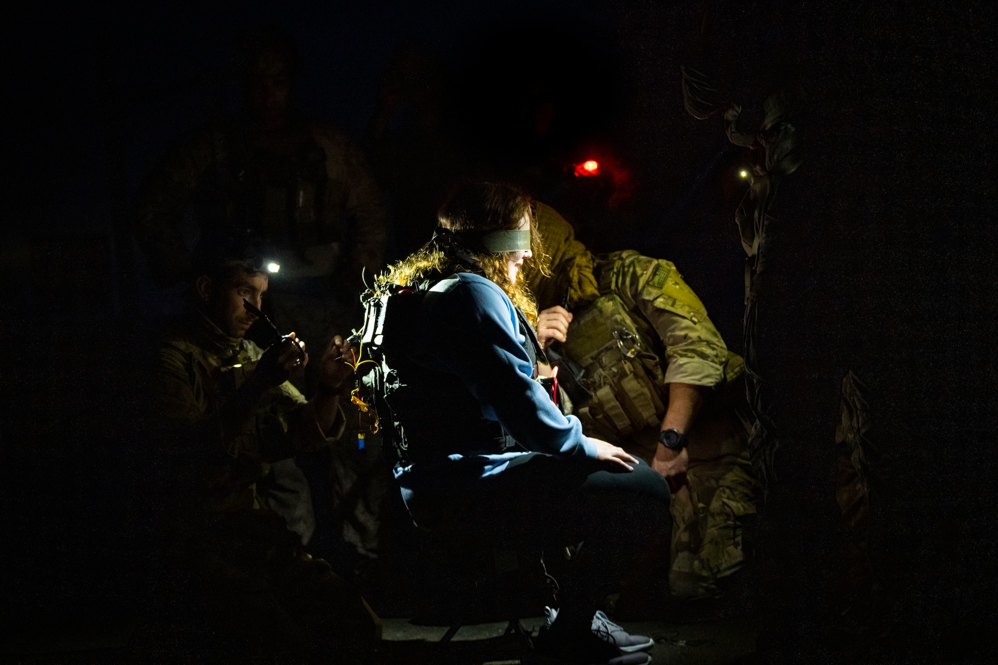 U.S. military members hold flashlights while disarming a suicide vest on a volunteer.