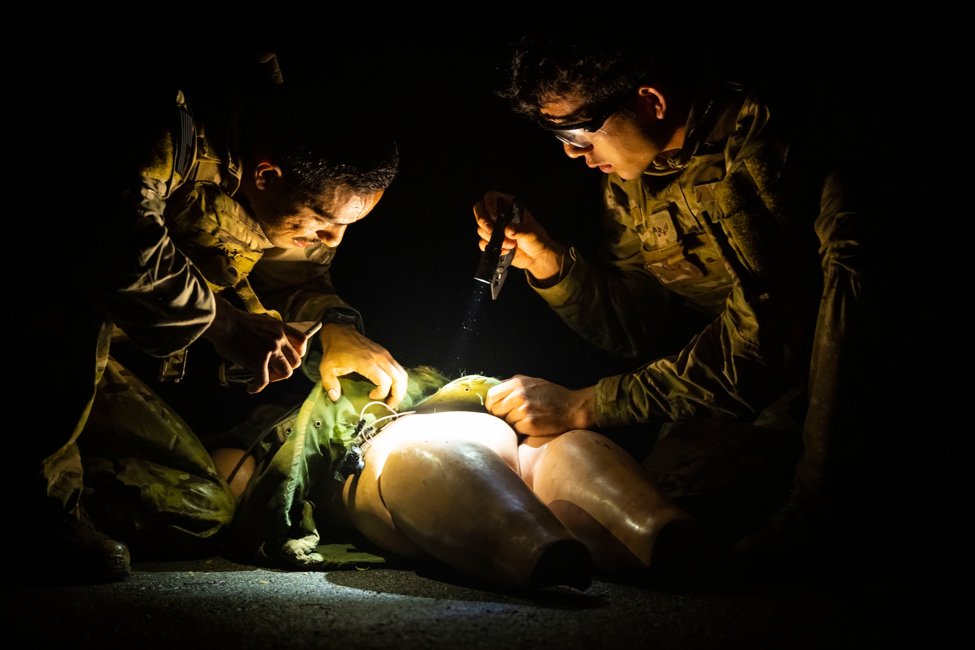 U.S. military members hold flashlights while disarming a suicide vest on a mannequin.