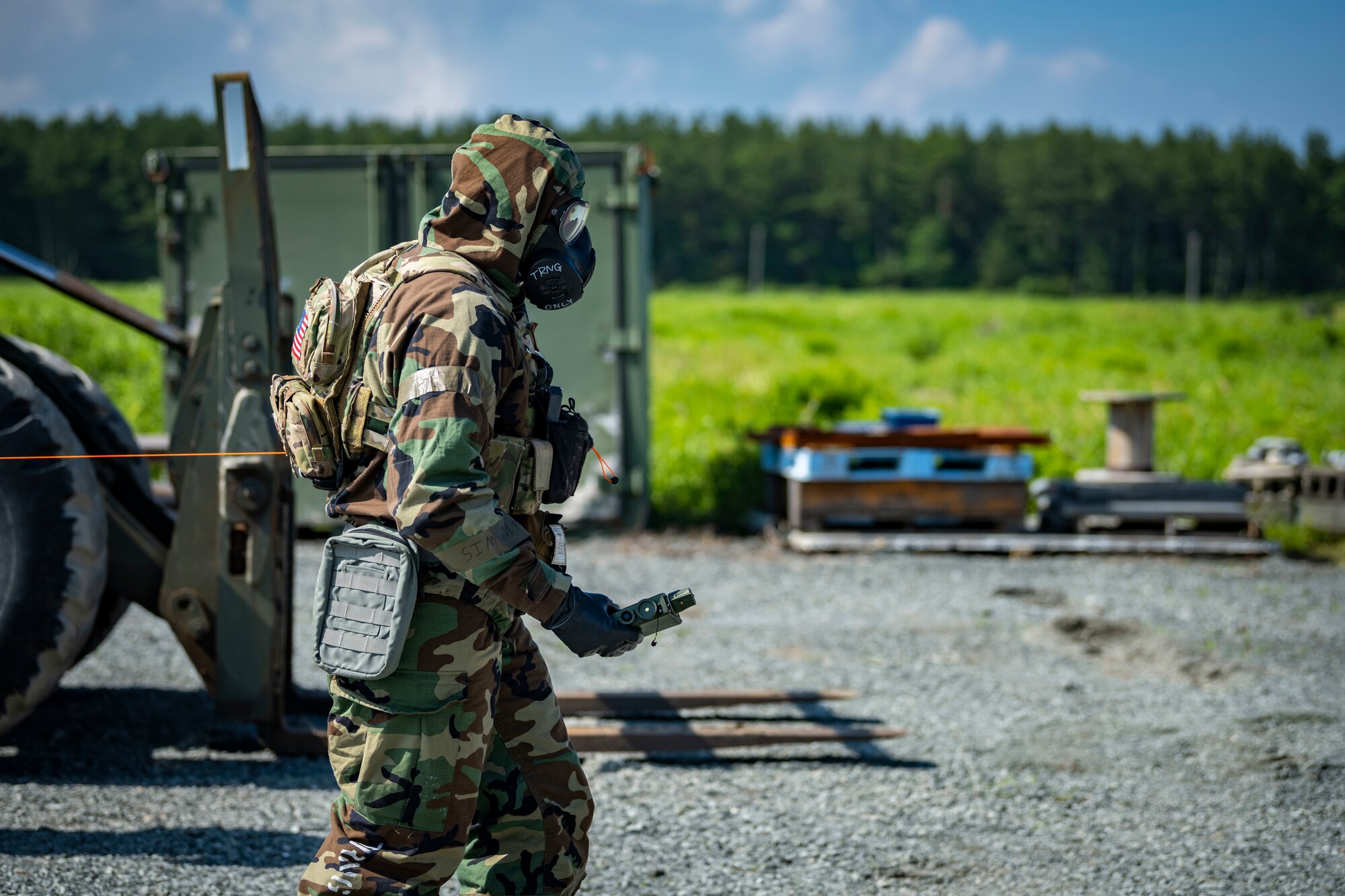 U.S. military member in chemical gear walks towards a chemical weapon with a joint chemical agent detector.