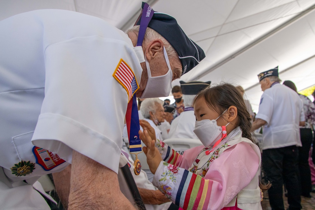 A young girl presents a medal to an older veteran.